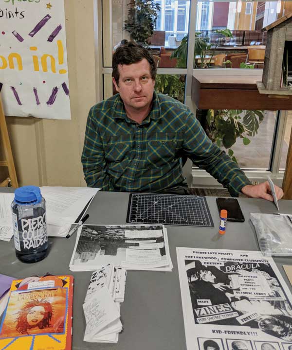 Jason Sloan outside of the library with examples of zines made by students and the community.